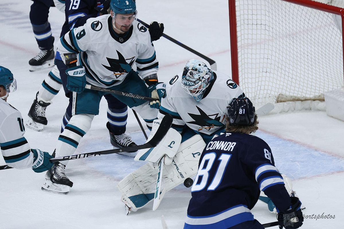 Several hockey players watch the puck as a San Jose Shark goalie makes a save